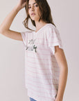 Side view of woman wearing Chaser’s white Mon Amour Stripe Tee with French slogan “mon amour” and light pink stripes on a plain background