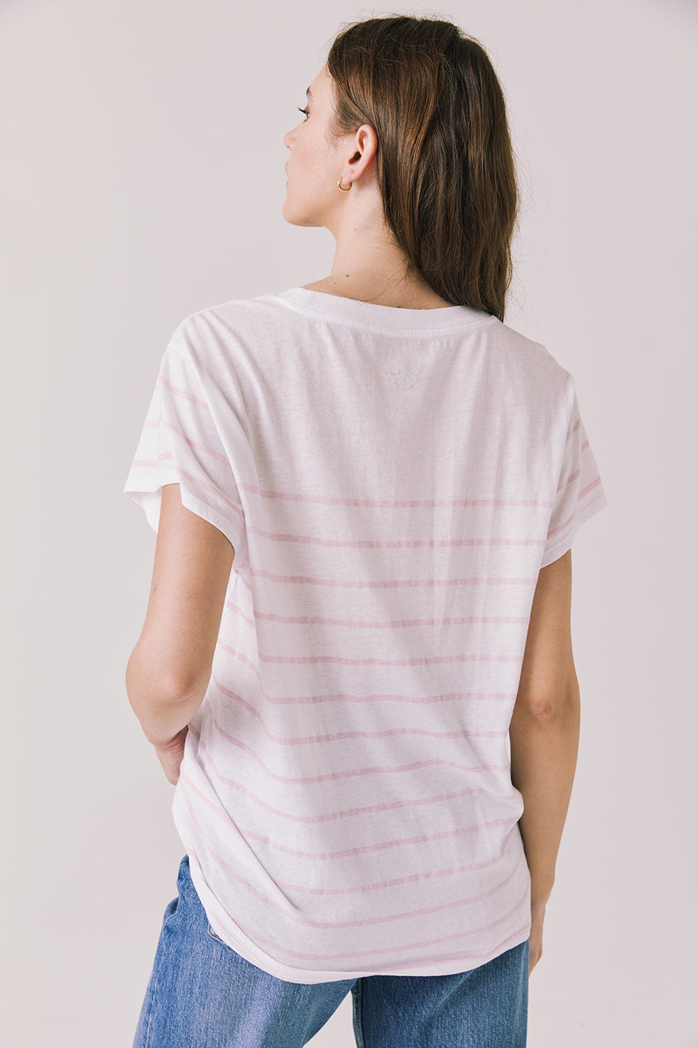 Back view of woman wearing Chaser’s white Mon Amour Stripe Tee with light pink stripes on a plain background