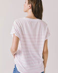 Back view of woman wearing Chaser’s white Mon Amour Stripe Tee with light pink stripes on a plain background