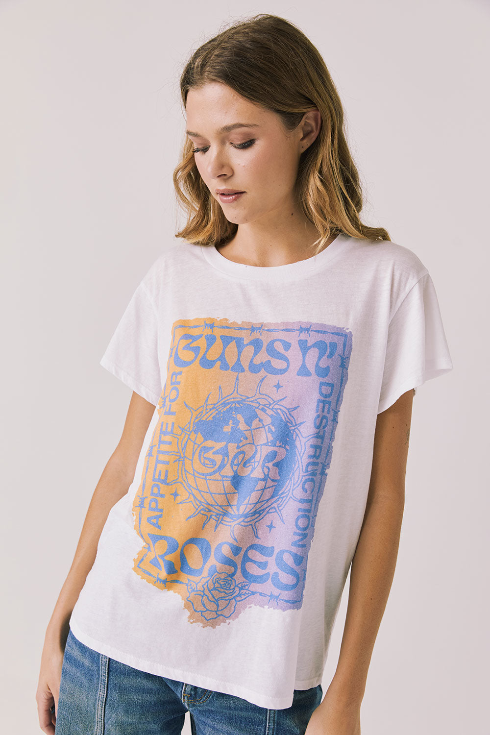 Front view of woman wearing Chaser’s white Guns N’ Roses World Tour Tee with colorful tour graphic (licensed band collaboration) on a plain background