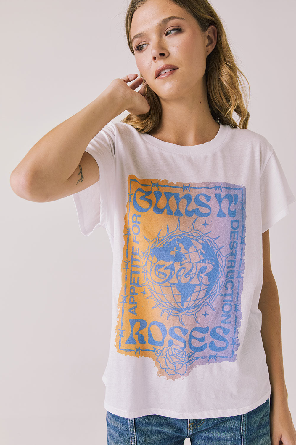 Front view of woman wearing Chaser’s white Guns N’ Roses World Tour Tee with colorful tour graphic (licensed band collaboration) on a plain background