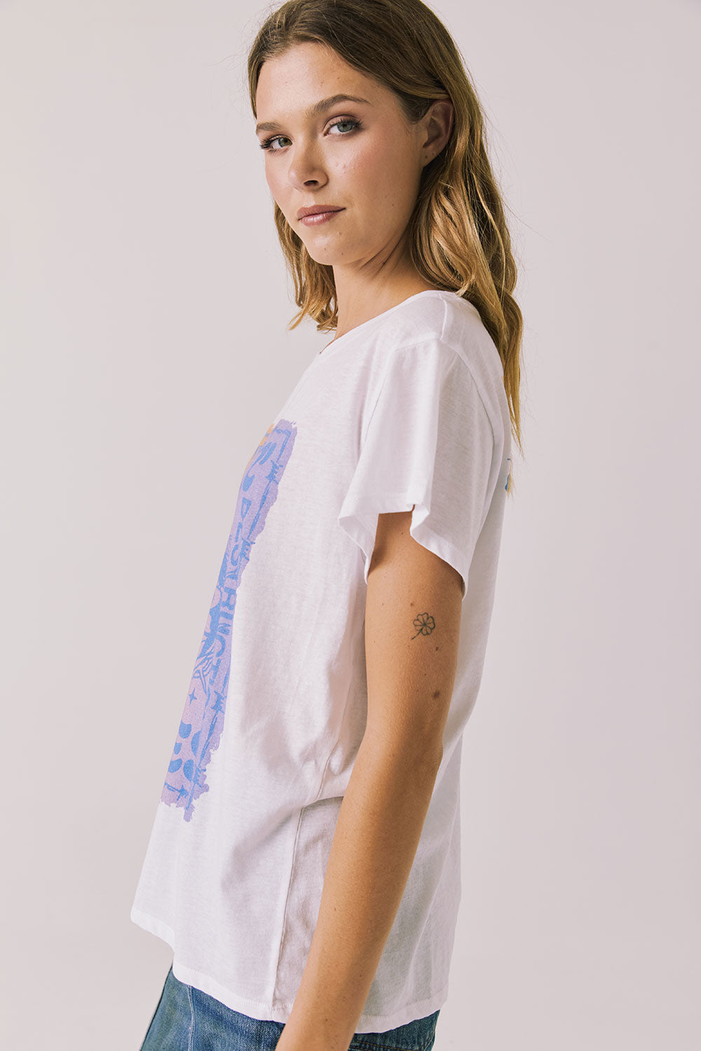 Side view of woman wearing Chaser’s white Guns N’ Roses World Tour Tee with colorful tour graphic (licensed band collaboration) on a plain background