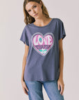 Front view of woman wearing Chaser’s slate blue Woodstock Love Revolution Tee with pink heart design and ‘LOVE’ text on a plain background (licensed music collaboration)