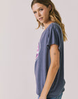 Side view of woman wearing Chaser’s slate blue Woodstock Love Revolution Tee showing pink heart and text detail on a plain background (licensed music collaboration)