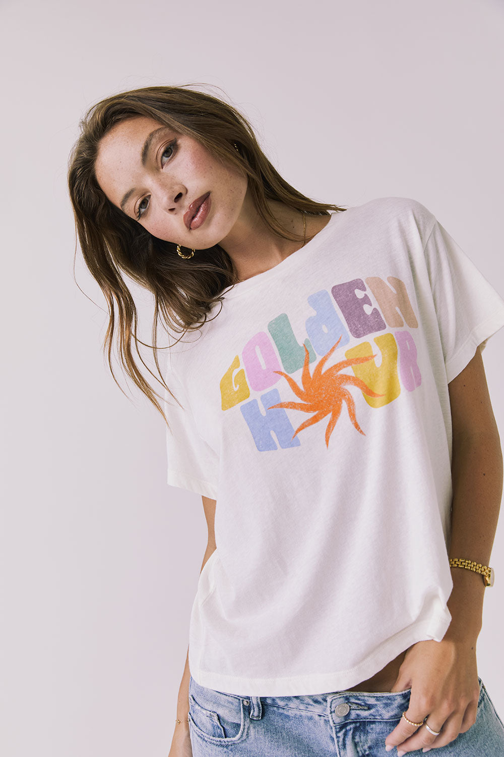 Front view of a woman wearing Chaser's white Golden Hour Tee with colorful graphic design on a plain background
