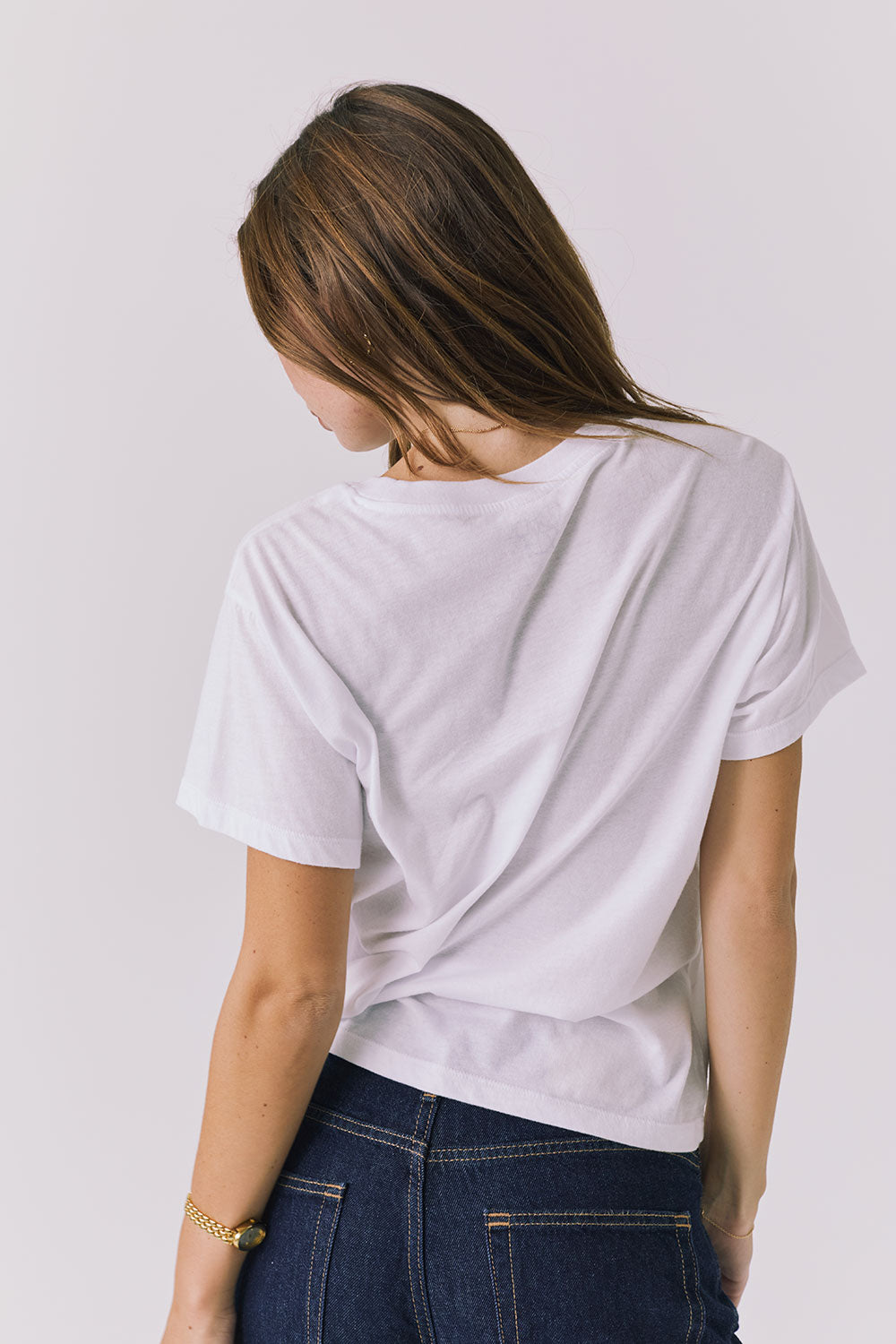 Back view of a woman wearing Chaser's white Golden Hour Tee on a plain background