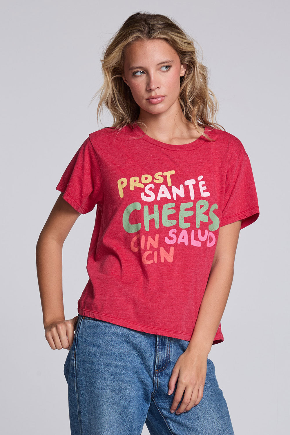 Model wearing Chaser's Cheers Tee in Cherry Bomb red with French-style celebratory lettering, angled view