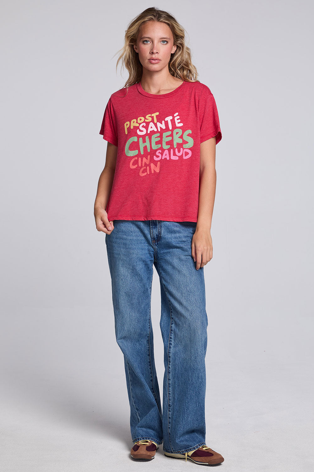 Model wearing Chaser's Cheers Tee in Cherry Bomb red with French-style celebratory lettering, full-body view