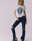 Full front view of a woman wearing Chaser's white Journey 1980 Tour Tee with a colorful graphic design and ripped denim on a plain background