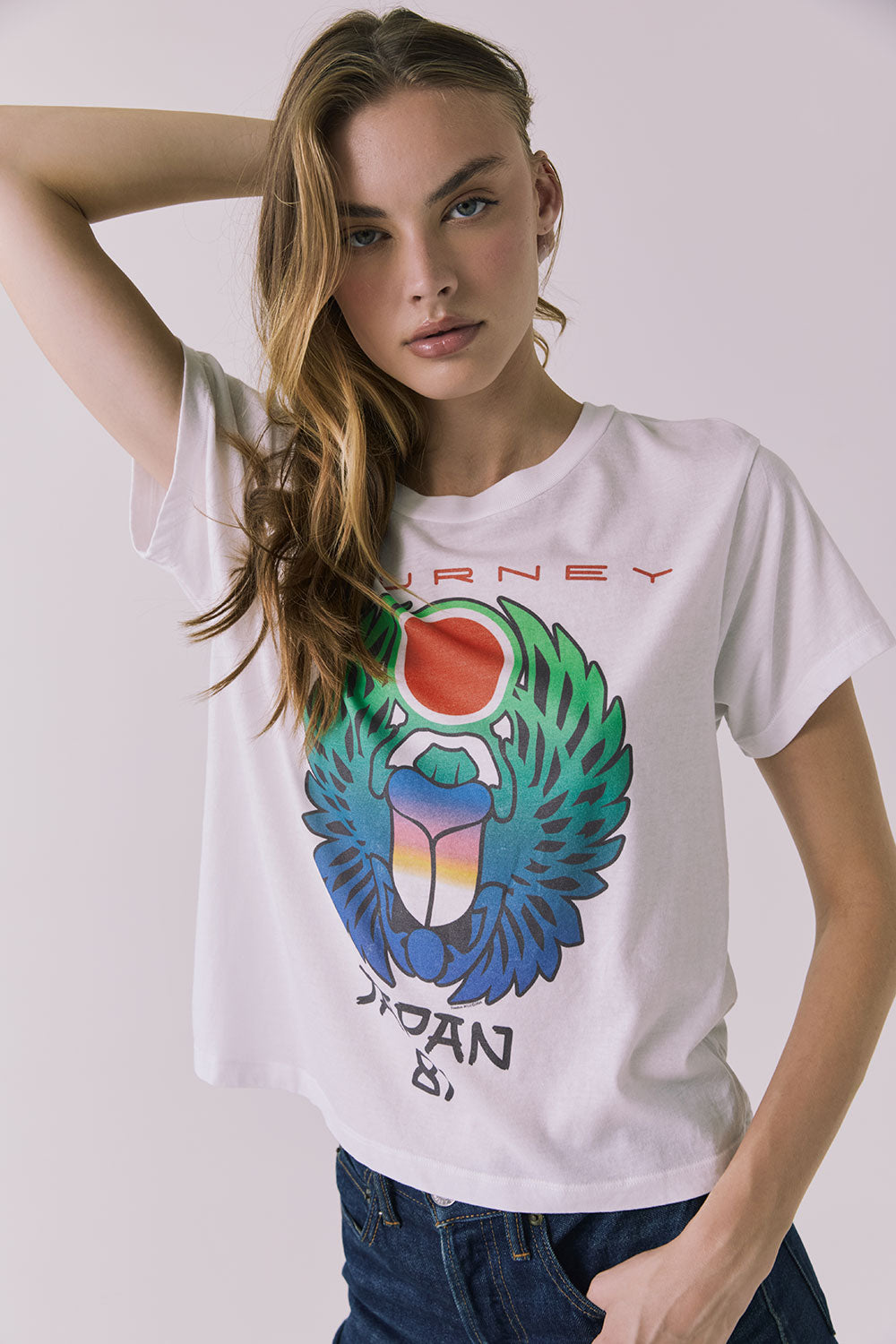 Front view of a woman wearing Chaser's white Journey 1980 Tour Tee with a colorful graphic design on a plain background