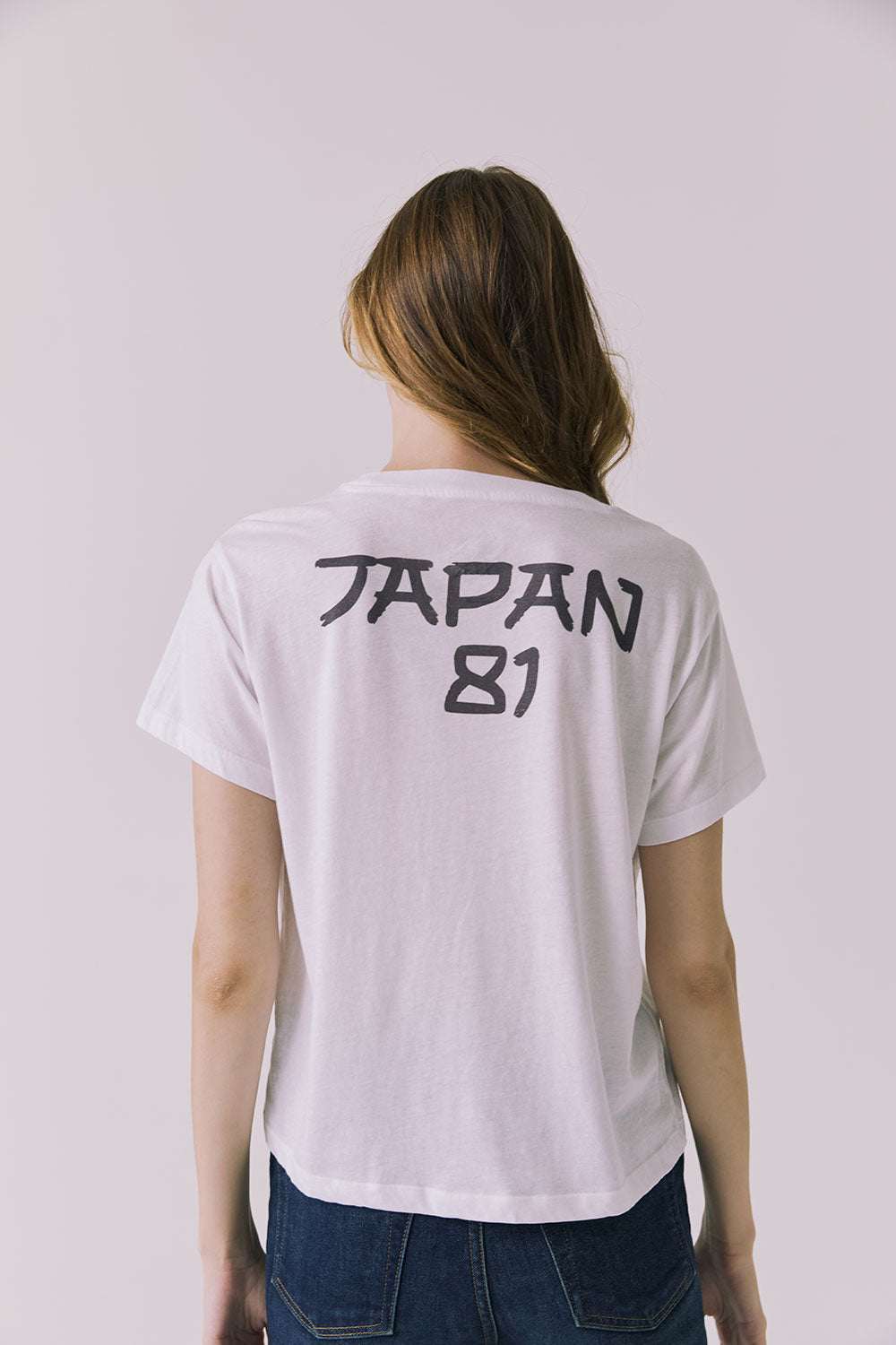 Back view of a woman wearing Chaser's white Journey 1980 Tour Tee with Japan 81 text on a plain background