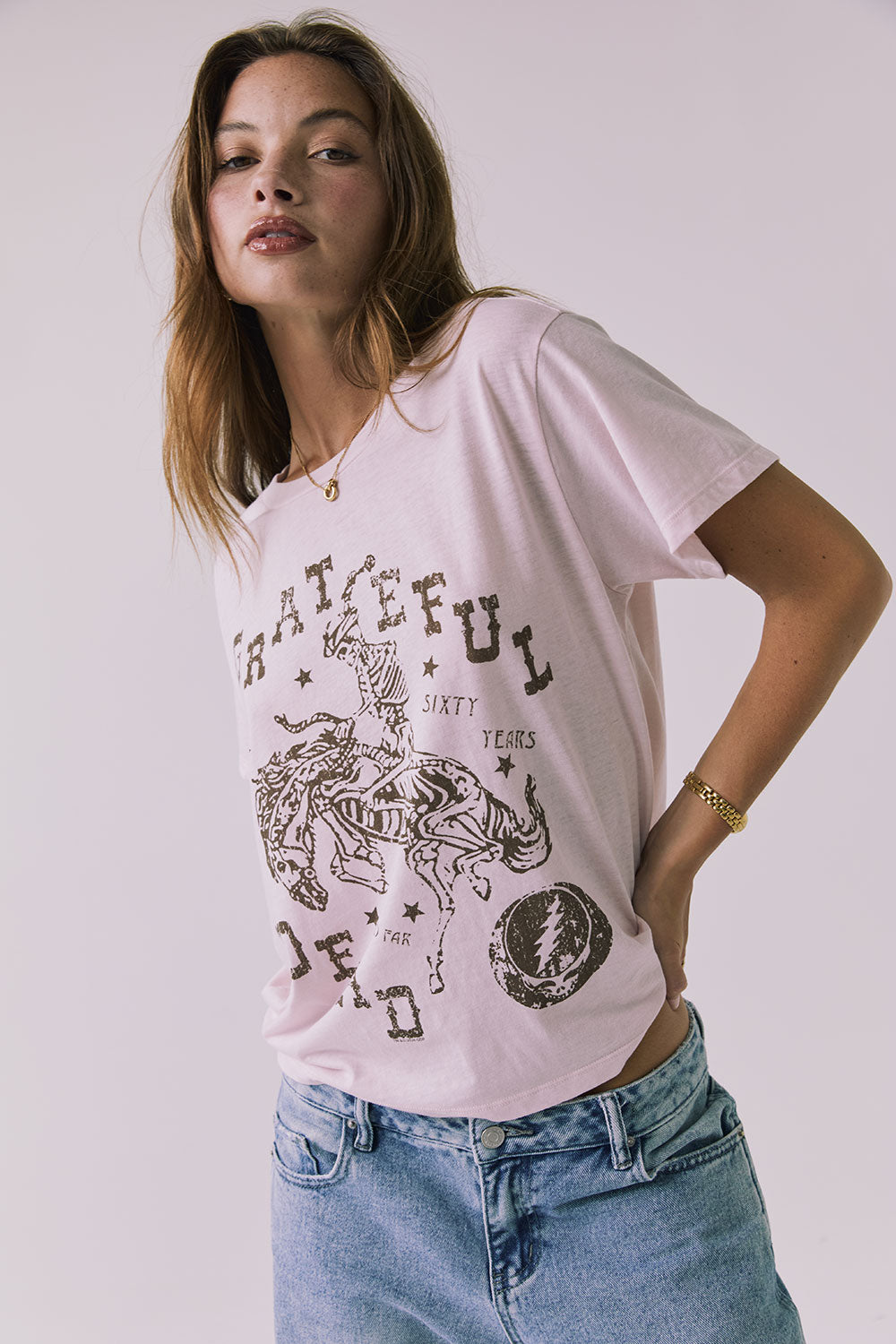 3/4 view of a woman wearing Chaser's the Grateful Dead 60 Years so Far pink tee with a graphic design on a plain background