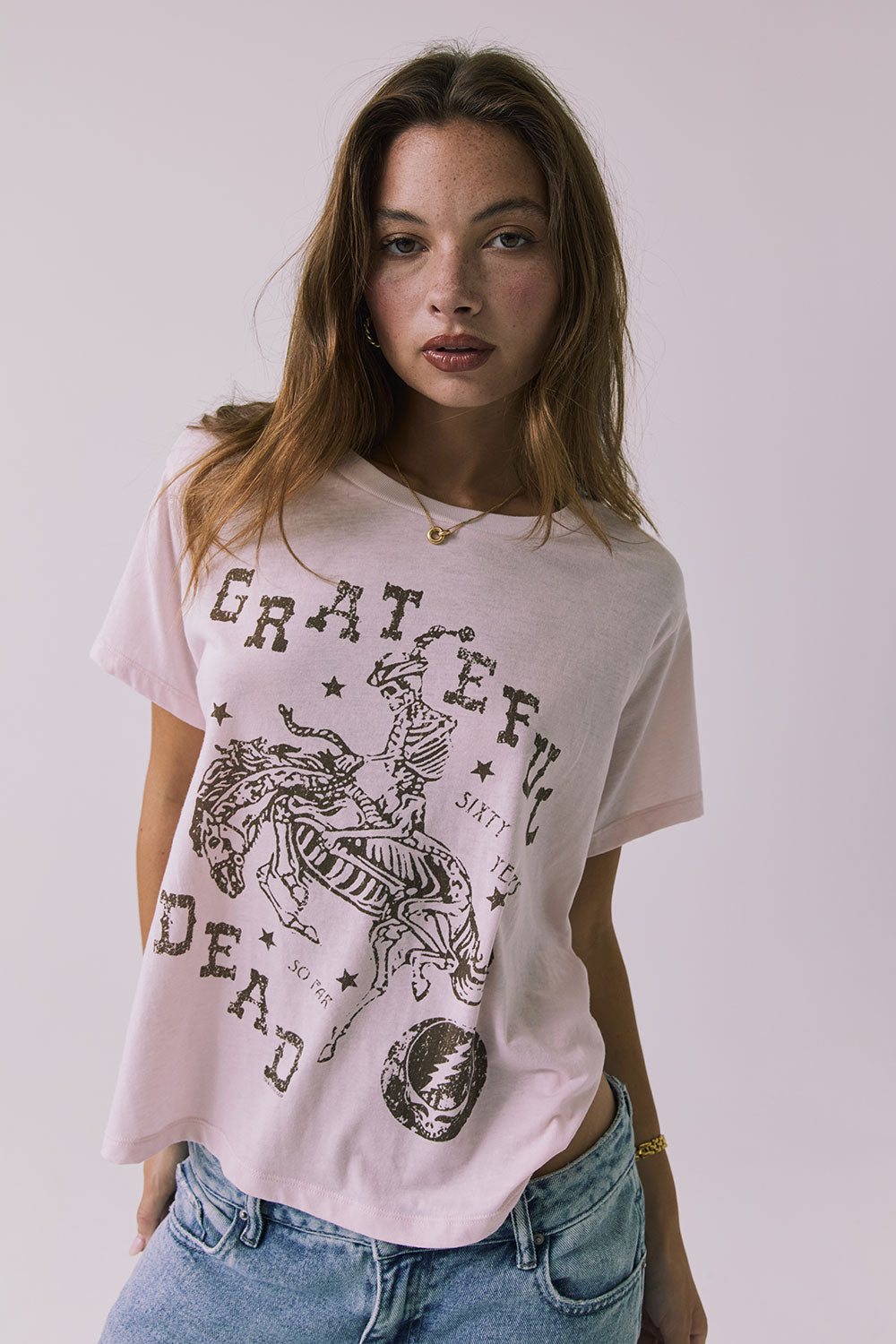 Front view of a woman wearing Chaser's the Grateful Dead 60 Years so Far pink tee with a graphic design on a plain background