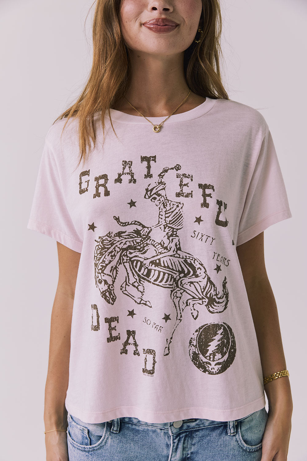 Close up view of a woman wearing Chaser's the Grateful Dead 60 Years so Far pink tee with a graphic design on a plain background