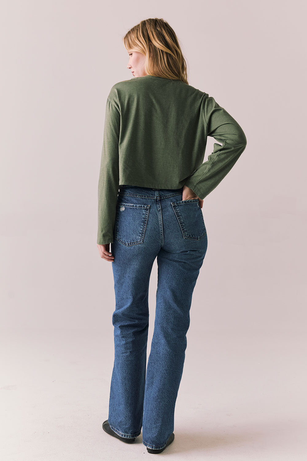 Back full view of womens wearing Chaser's Classics Motors washed bronze green long sleeve with retro graphic and denim on a plain background