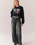 Full body view of model wearing AC/DC UK Tour ’80 Tee in True Black with cropped long-sleeve fit and vintage tour poster graphic paired with jeans on plain background