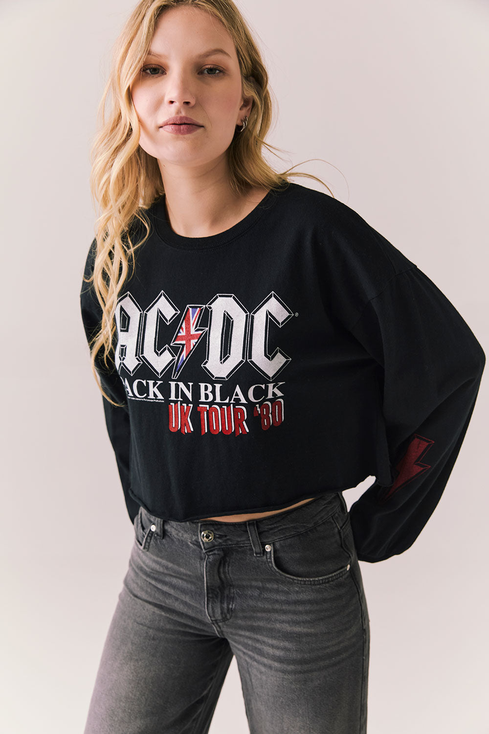 Side view of AC/DC UK Tour ’80 Tee in True Black with vintage UK Tour 1980 poster graphic and cropped long-sleeve fit on plain background