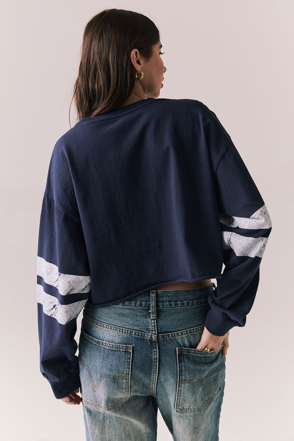 Back body view of model in Go Team long sleeve in blue with contrast cuff details and jeans on a plain background