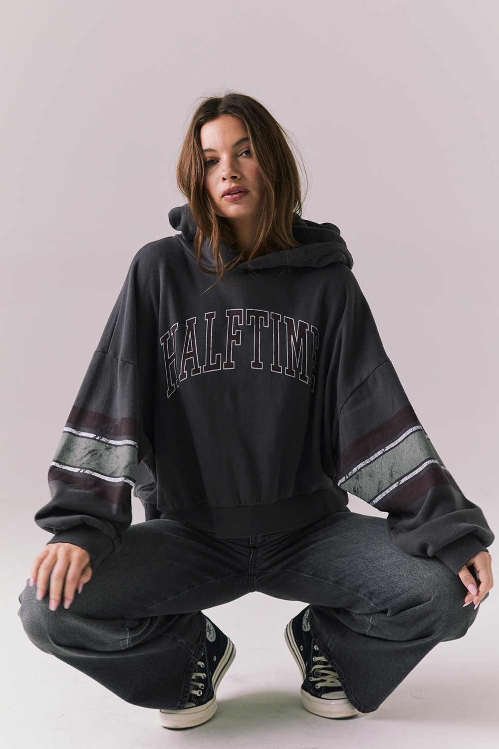 Full body view of model wearing the Halftime fleece pullover hoodie in True Black with ‘HALFTIME’ chest graphic, crouching on the floor against a plain background.