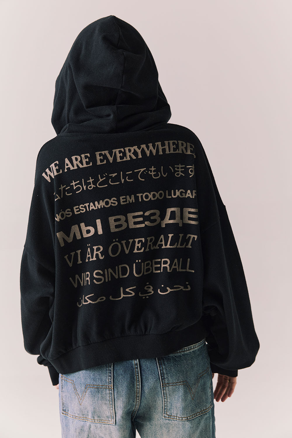 Back view of The Grateful Dead We Are Everywhere Hoodie in True Black with cropped boxy fit, hood up, and skull graphic made from stars and zodiac signs against a plain background