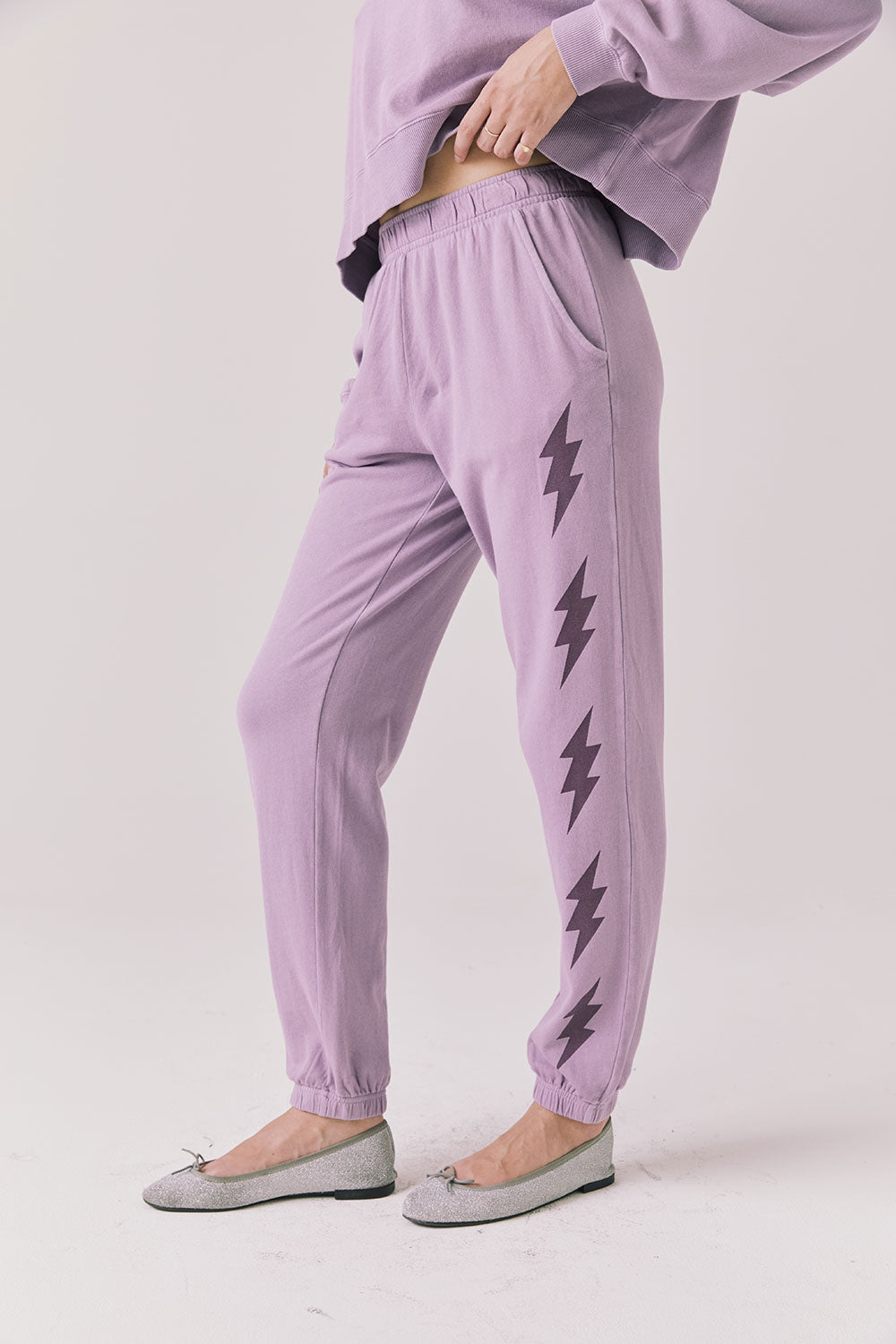 Side view of woman wearing Chaser’s Bolt Amethyst Purple Joggers with matching pullover on a plain background