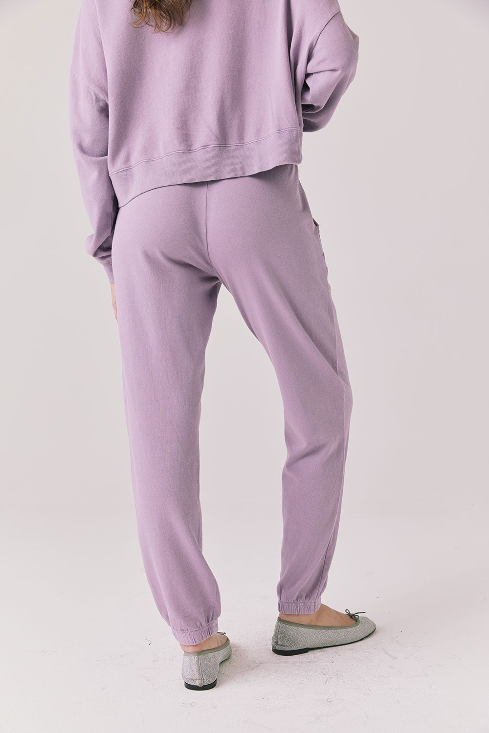Full body view of woman wearing Chaser’s Bolt Amethyst Purple Joggers with matching pullover on a plain background