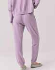Full body view of woman wearing Chaser’s Bolt Amethyst Purple Joggers with matching pullover on a plain background