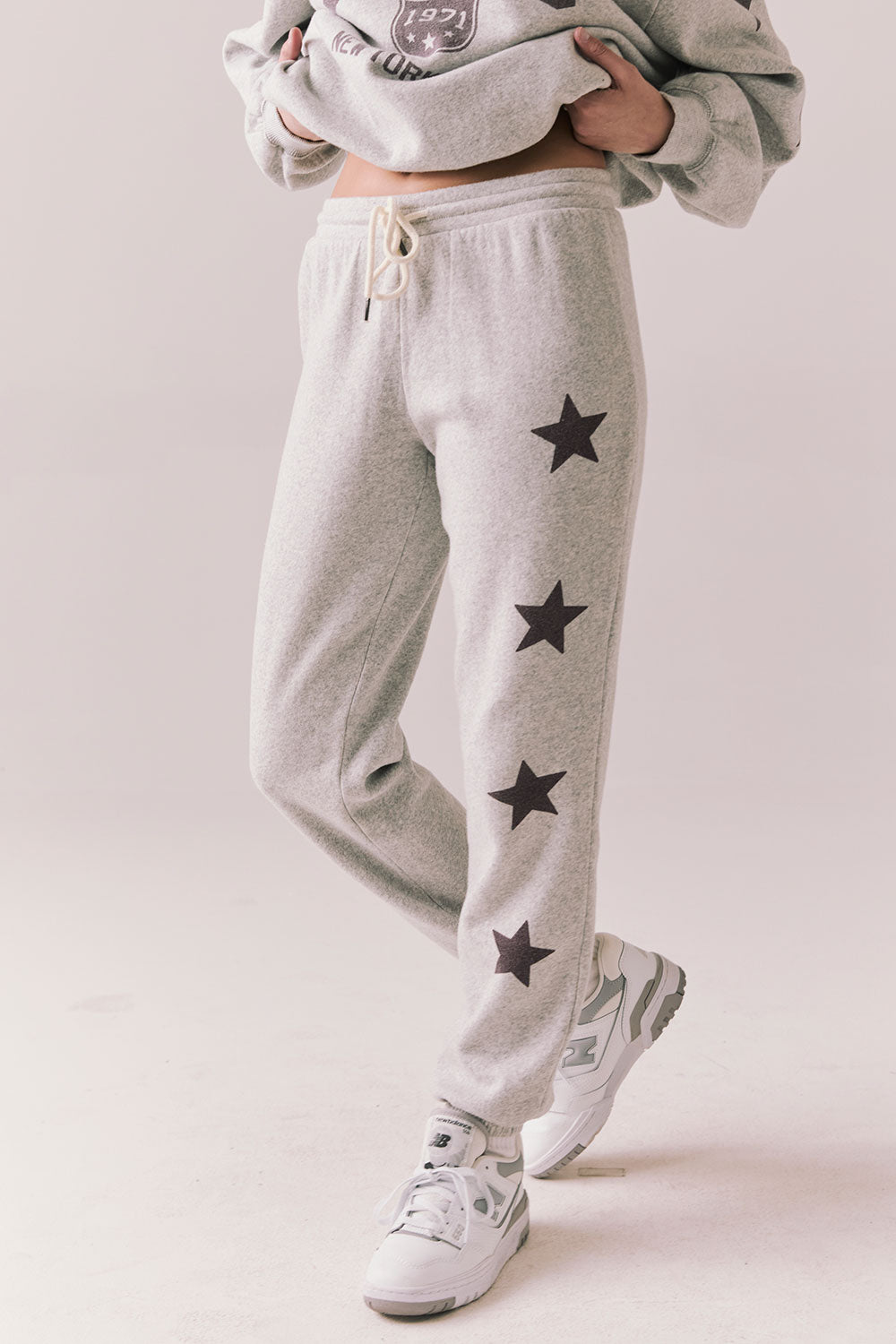 Side view of NYC Stars Joggers in Heather Grey with black star print down each leg, styled for a casual lounge look, against a plain background
