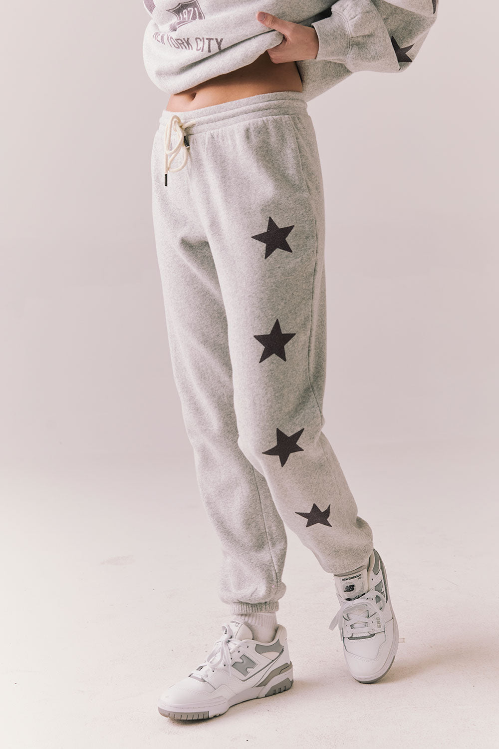 Side view of NYC Stars Joggers in Heather Grey with black star print down each leg, styled for a casual lounge look, against a plain background