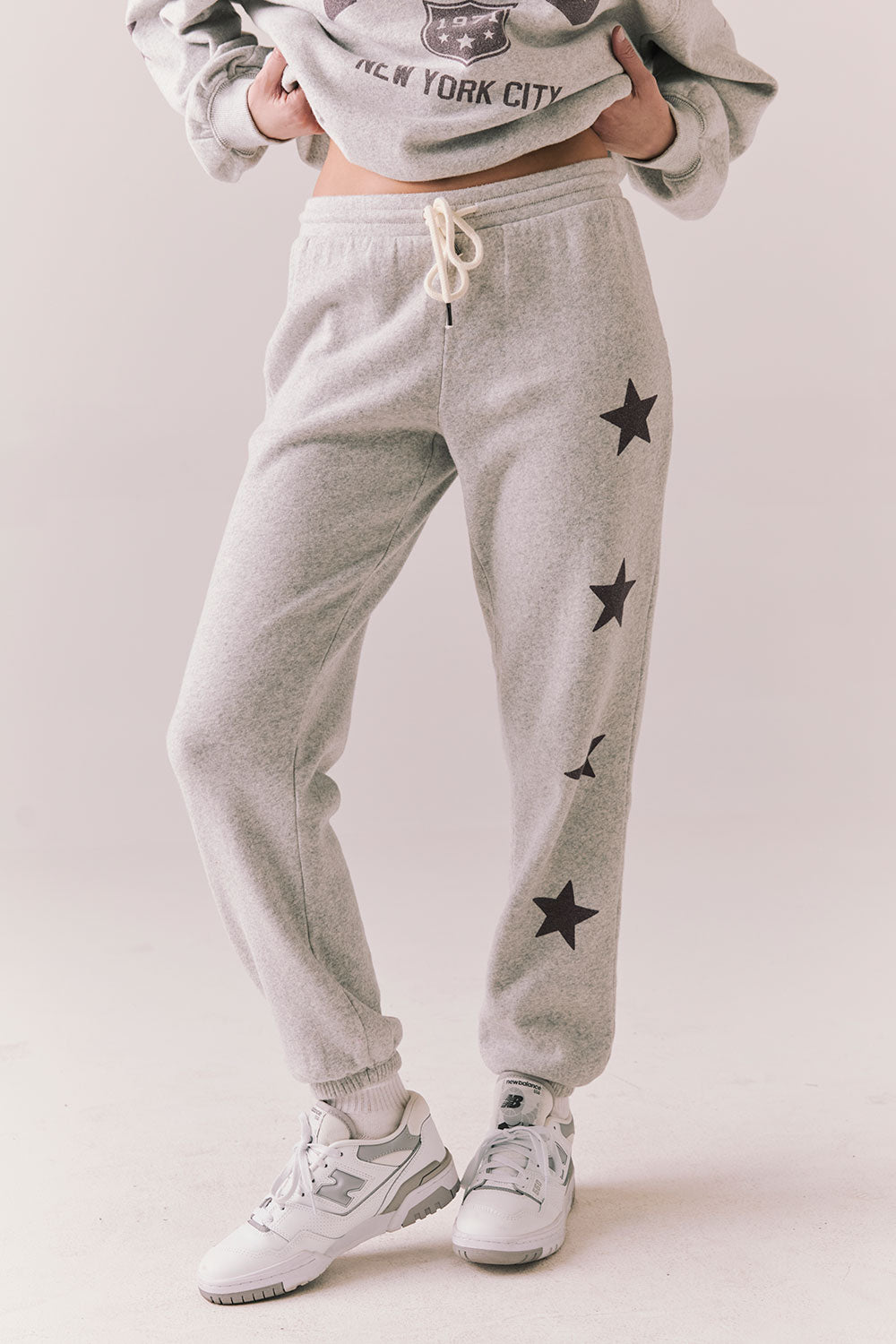 Side view of NYC Stars Joggers in Heather Grey with black star print down each leg, styled for a casual lounge look, against a plain background
