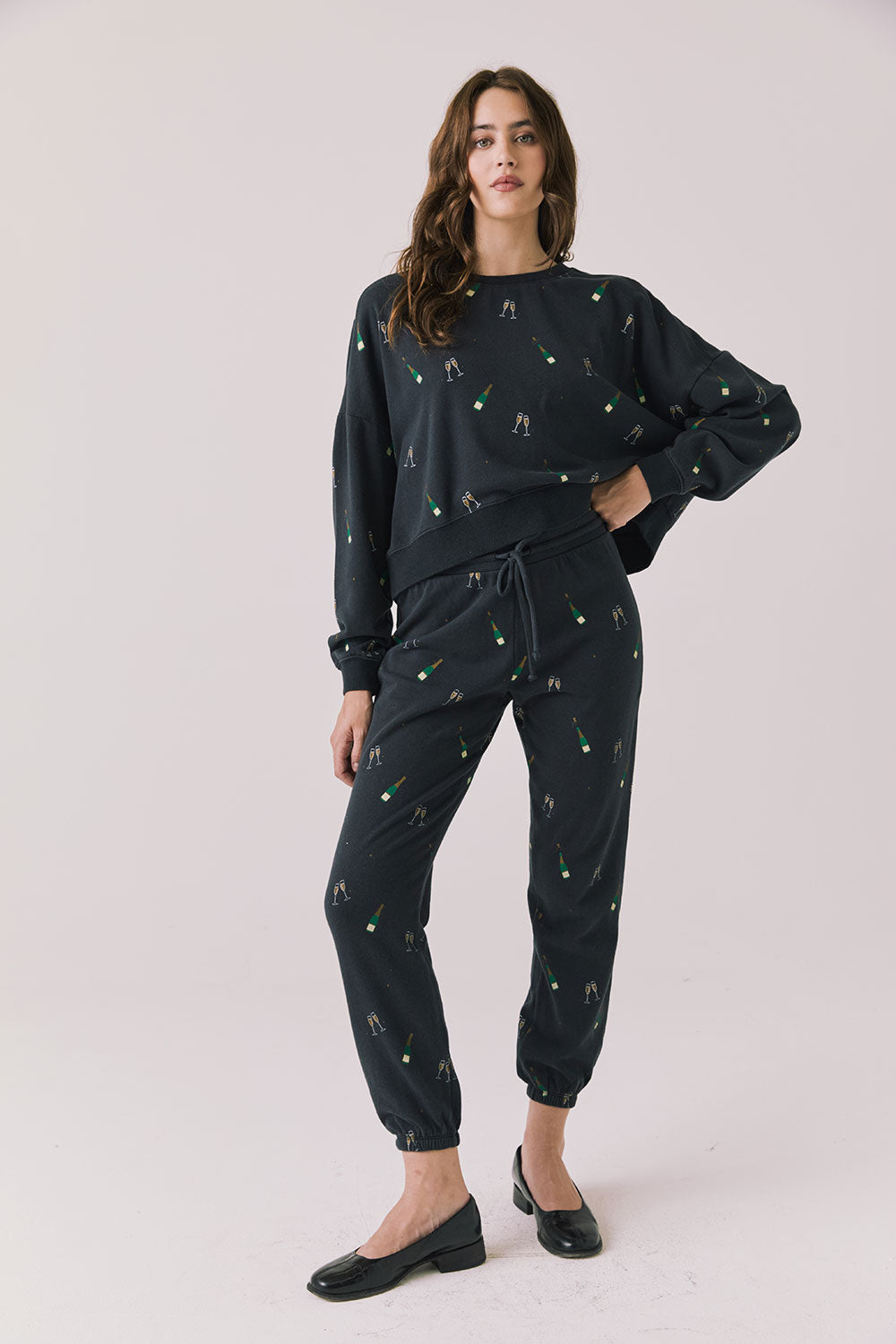 Full body view of woman wearing Chaser’s black Champagne Party Joggers with matching Champagne Party Pullover on a light grey background