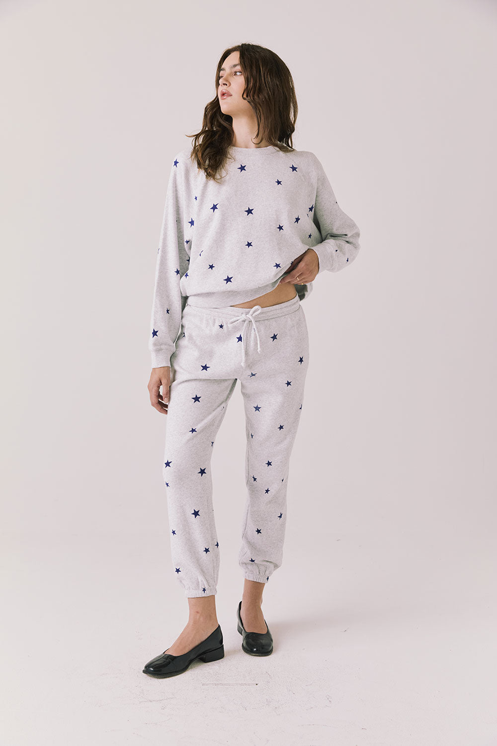 Full body view of woman wearing Chaser’s Festive Stars Joggers in light grey with star patterns and matching top on a white background