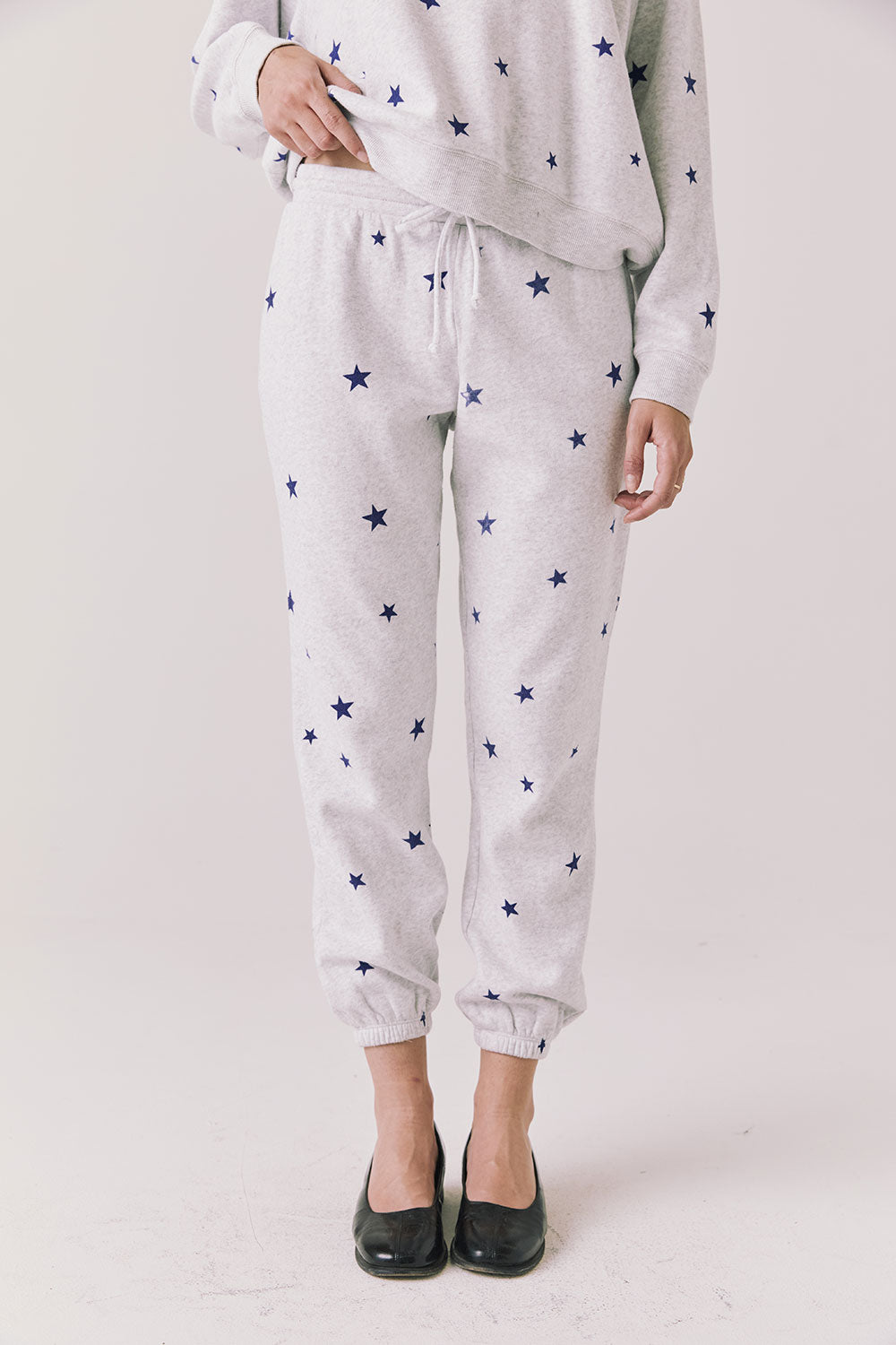 Full body view of woman wearing Chaser’s Festive Stars Joggers in light grey with star patterns and matching top on a white background