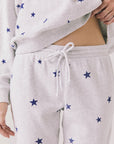 Full body view of woman wearing Chaser’s Festive Stars Joggers in light grey with star patterns and matching top on a white background