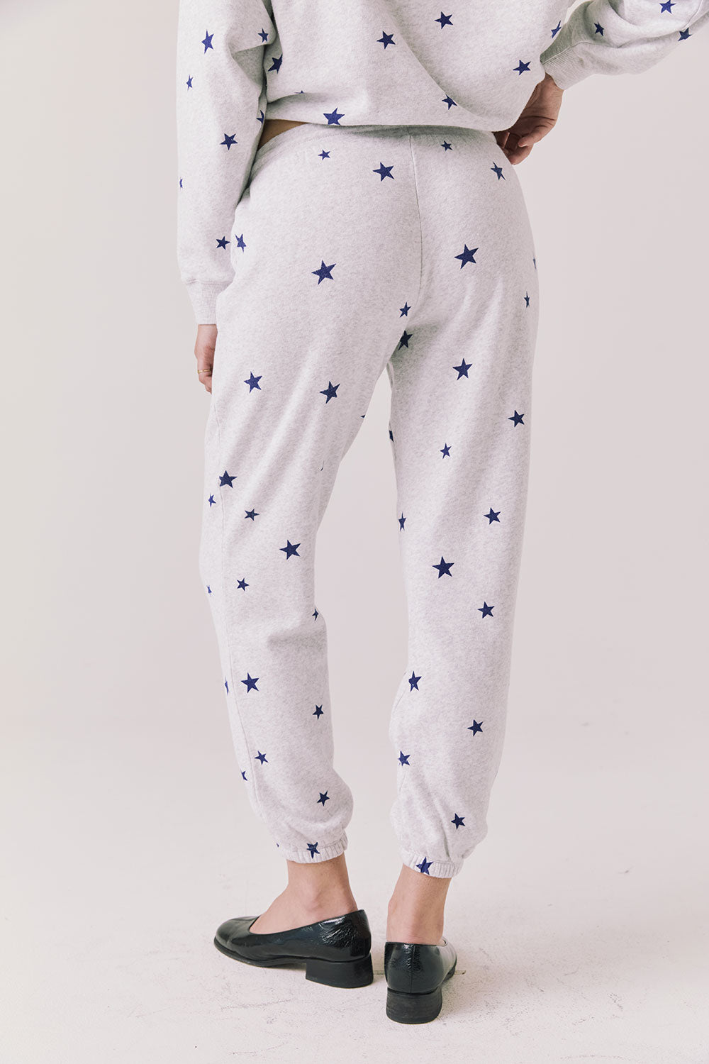 Back view of woman wearing Chaser’s Festive Stars Joggers in light grey with star patterns on a white background