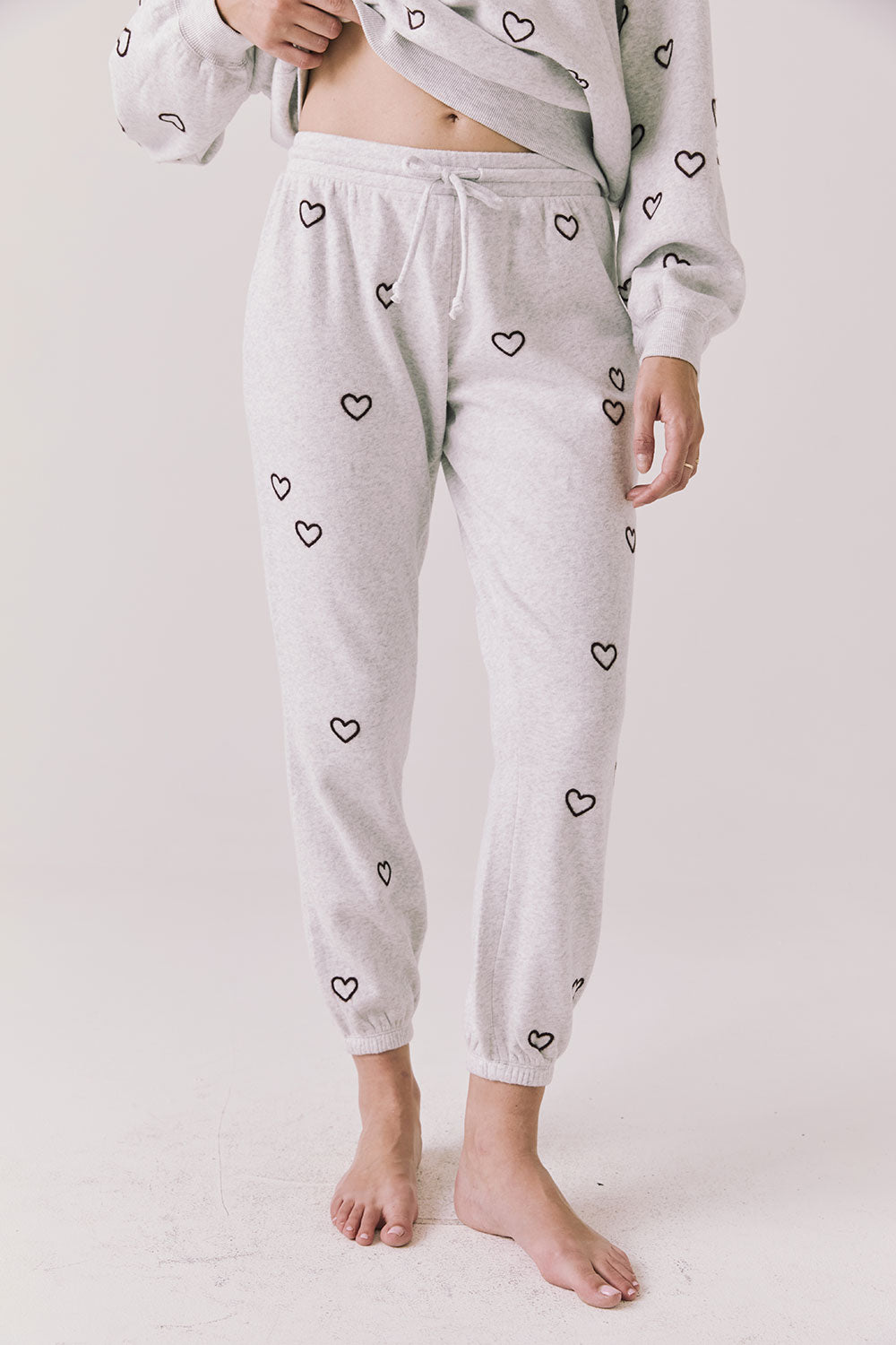 Front view of woman wearing Chaser’s light grey Tossed Hearts Pants with small heart patterns on a white background