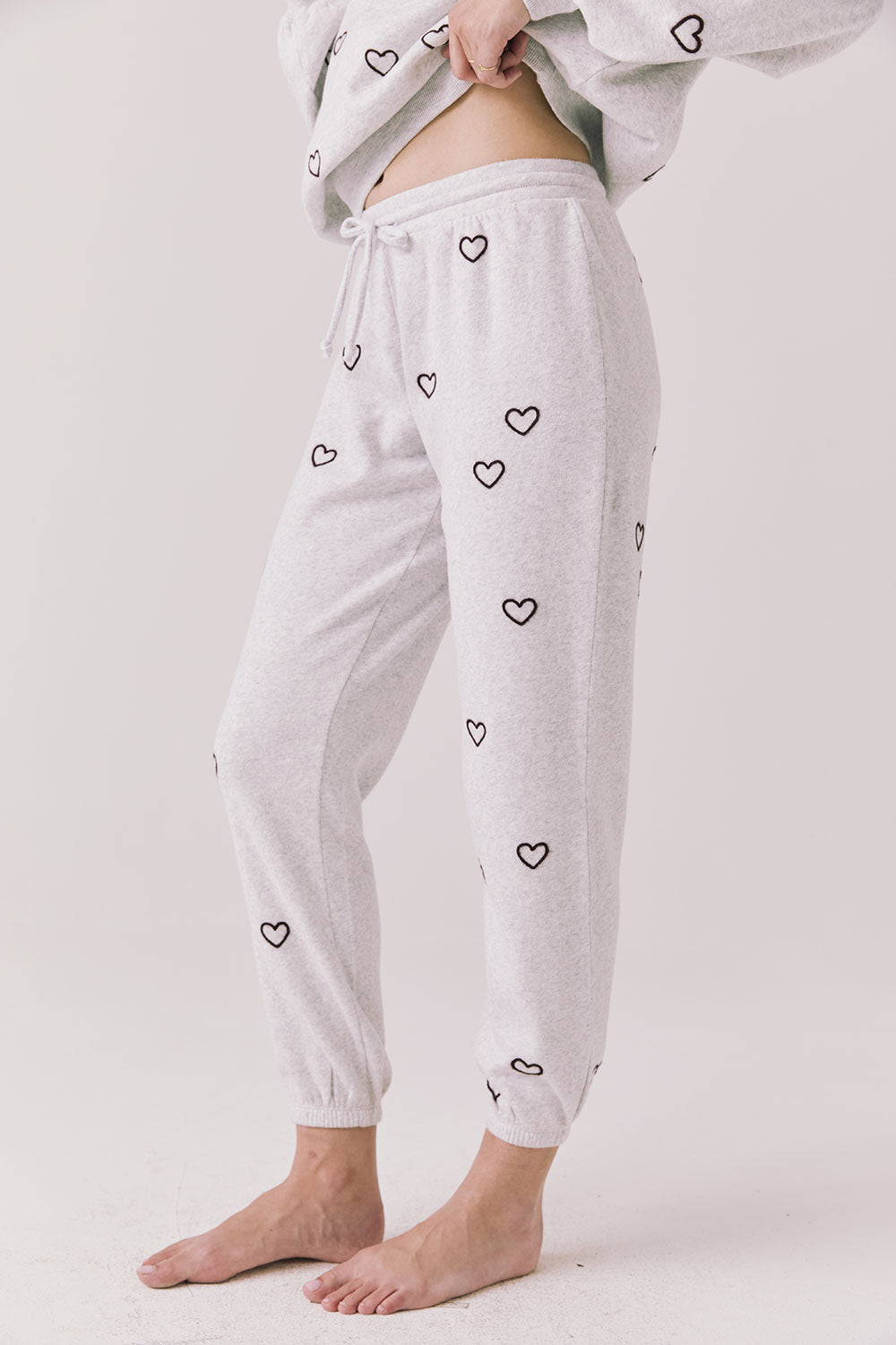 Side view of woman wearing Chaser’s light grey Tossed Hearts Pants with small heart patterns on a white background
