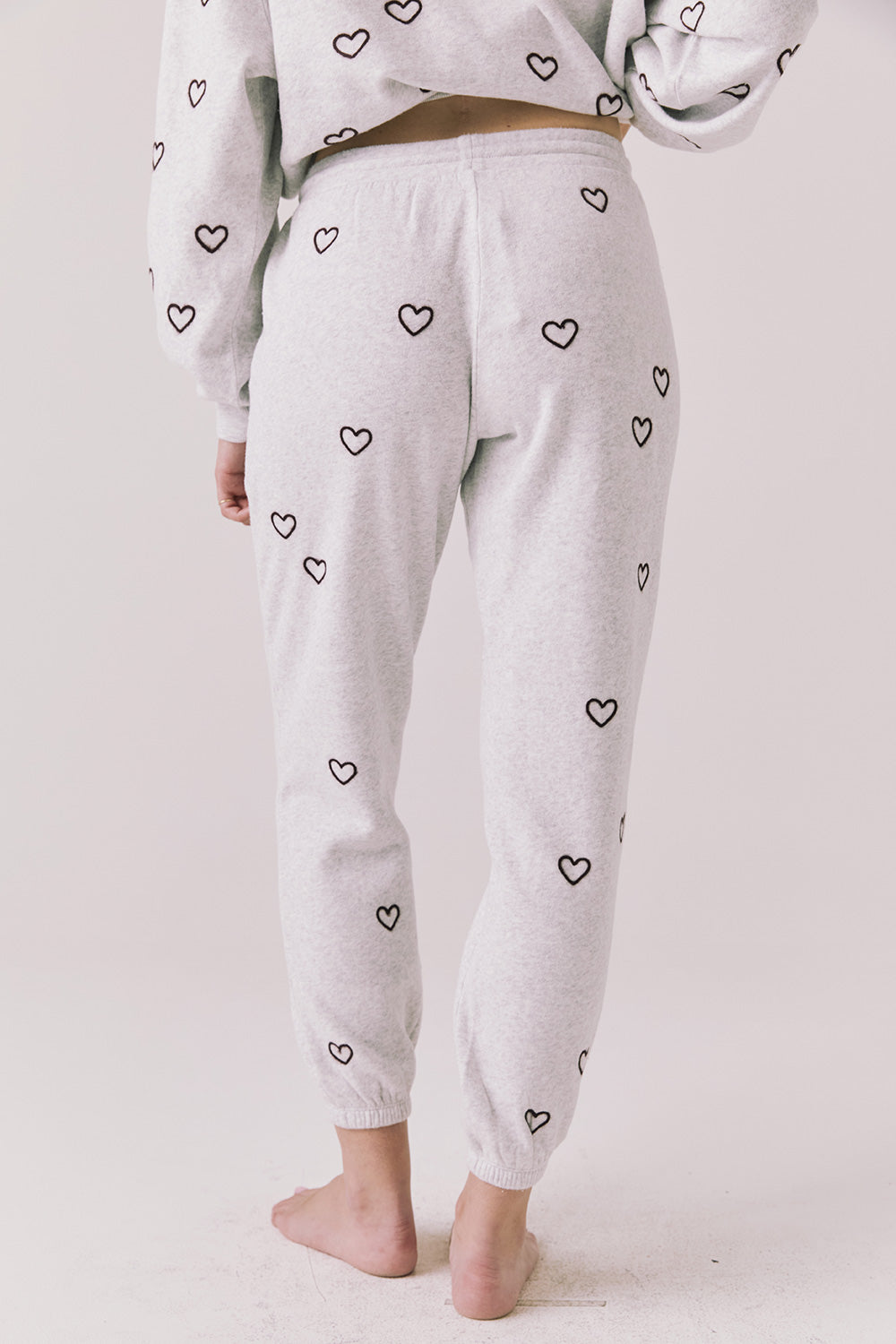 Back view of woman wearing Chaser’s light grey Tossed Hearts Pants with small heart patterns on a white background