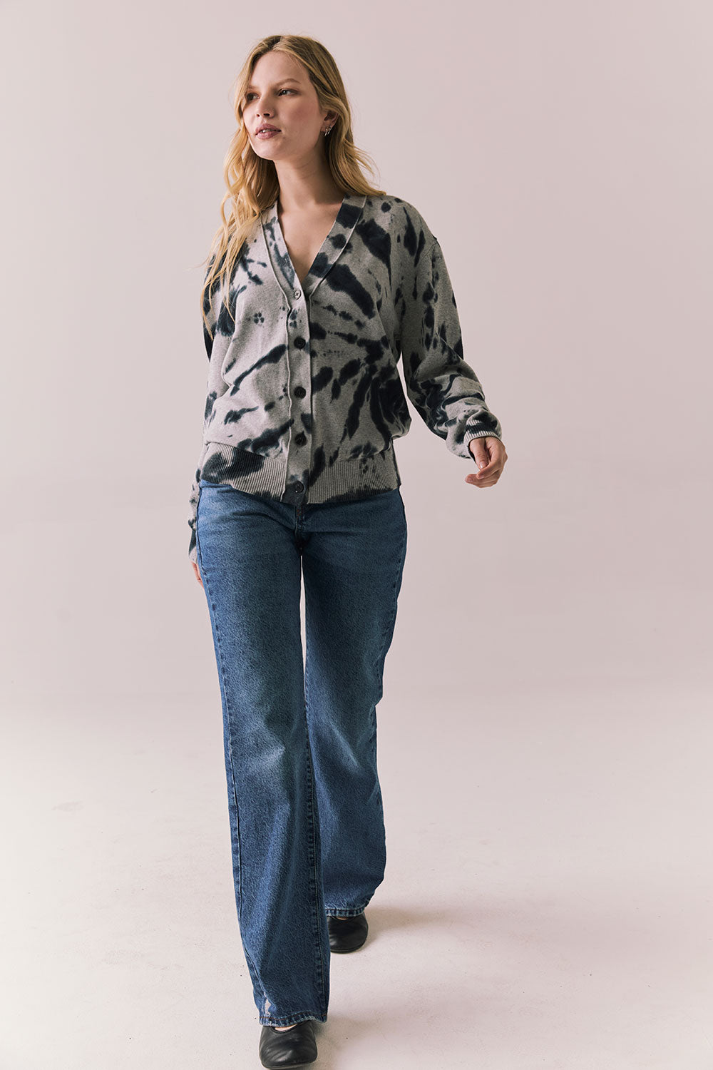 Full body view of model in black tie dye hoodie and blue jeans on a plain background