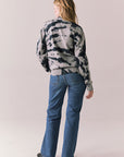 Back full body view of model in black tie dye hoodie and blue jeans on a plain background