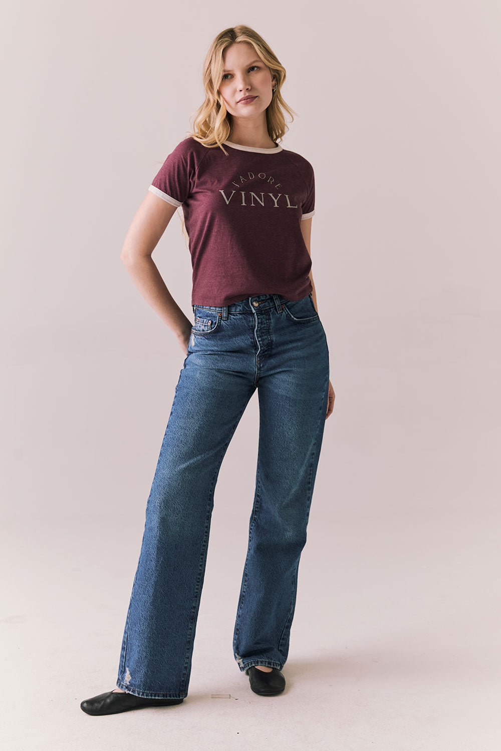 Full front view of model in J’adore Vinyl Tee in fig purple with cream ringer trim and vintage-style text and blue jeans on a plain background