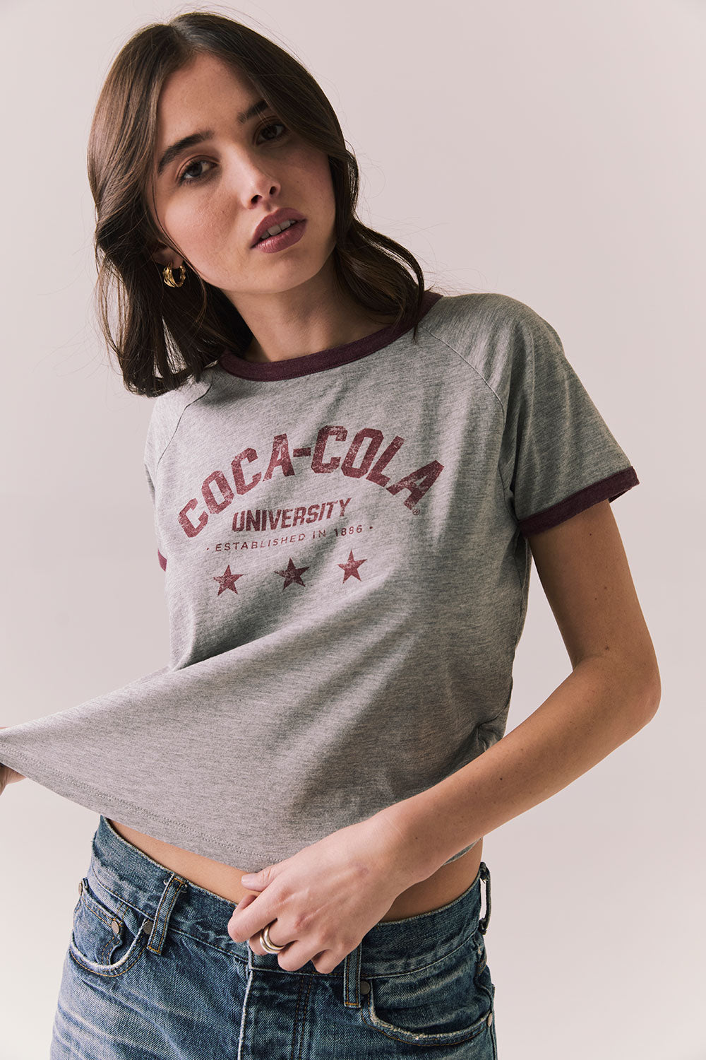 Woman wearing a gray 'Coca-Cola University' t-shirt with red text on a plain background