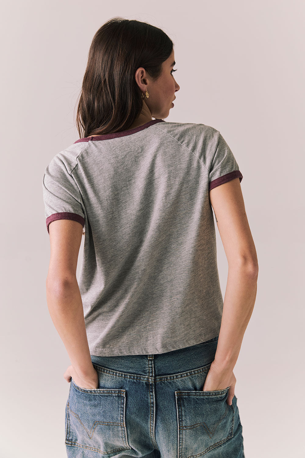 Back view of woman wearing a gray 'Coca-Cola University' t-shirt against a plain background
