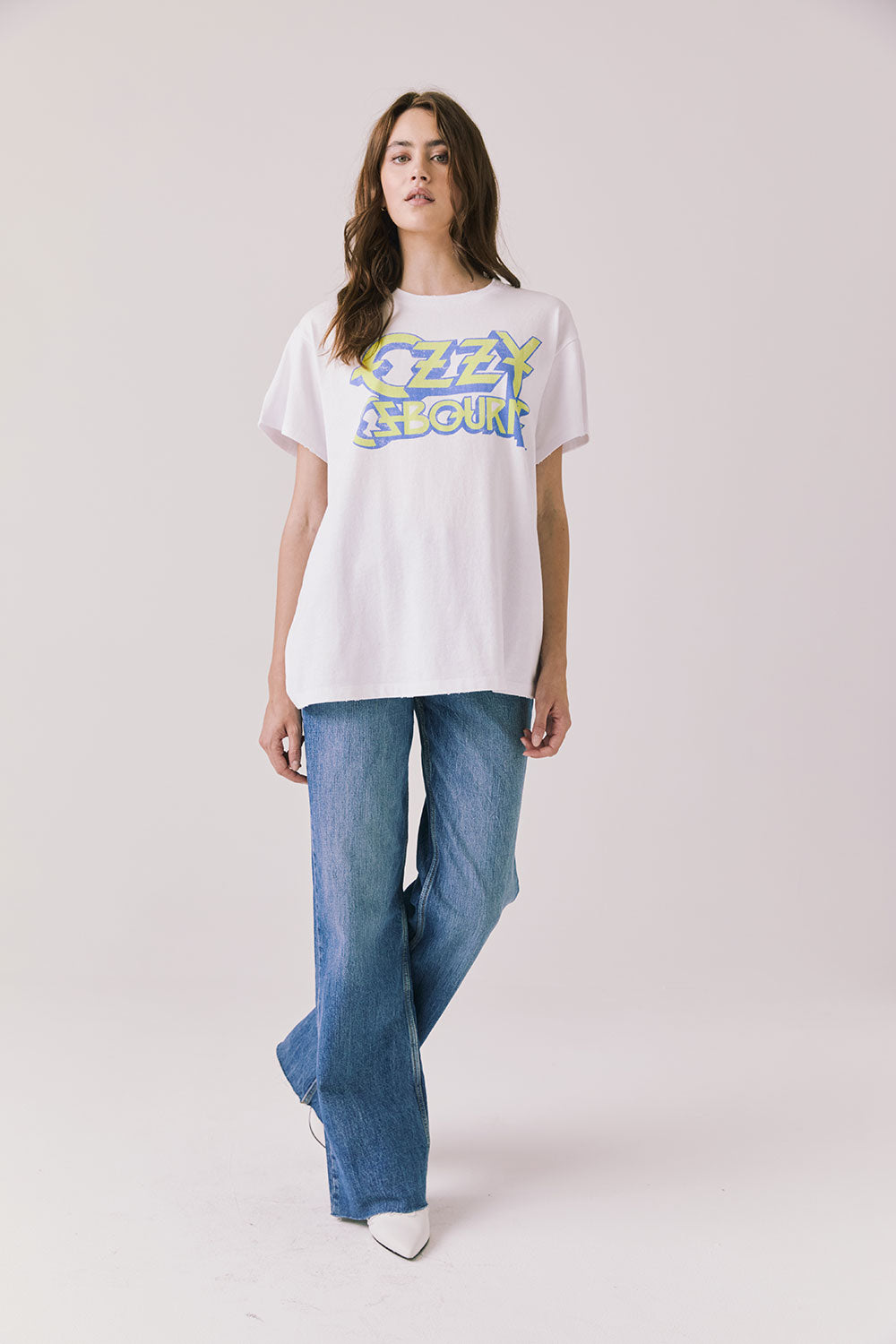 Full body view of woman wearing Chaser’s white Ozzy Osbourne Tour ’86 Tee and blue jeans on a plain background