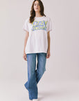 Full body view of woman wearing Chaser’s white Ozzy Osbourne Tour ’86 Tee and blue jeans on a plain background