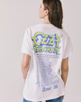 Back view of woman wearing Chaser’s white Ozzy Osbourne Tour ’86 Tee featuring “OZZY OSBOURNE” text, tour dates, and “TOUR 86” lettering on a plain background