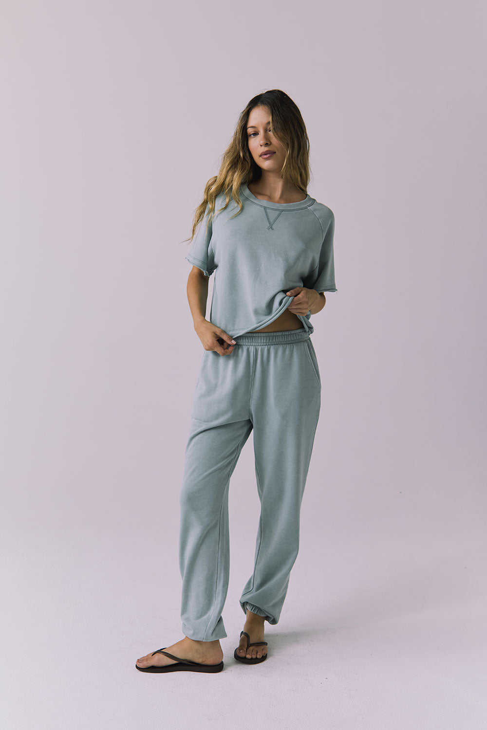 Full body view of woman wearing Chaser's Mission Joggers in garden green sage with the matching Amelia pullover on a plain background