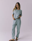 Full body view of woman wearing Chaser's Mission Joggers in garden green sage with the matching Amelia pullover on a plain background