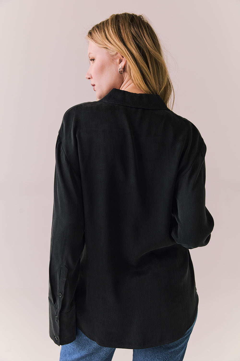 Back view of a model wearing the Helenaa button-down shirt in True Black with collared neckline and oversized silhouette, styled with relaxed jeans against a plain backdrop.