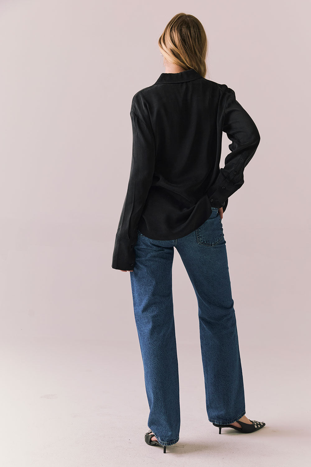 Back front view of a model wearing the Helenaa button-down shirt in True Black with collared neckline and oversized silhouette, styled with relaxed jeans against a plain backdrop.